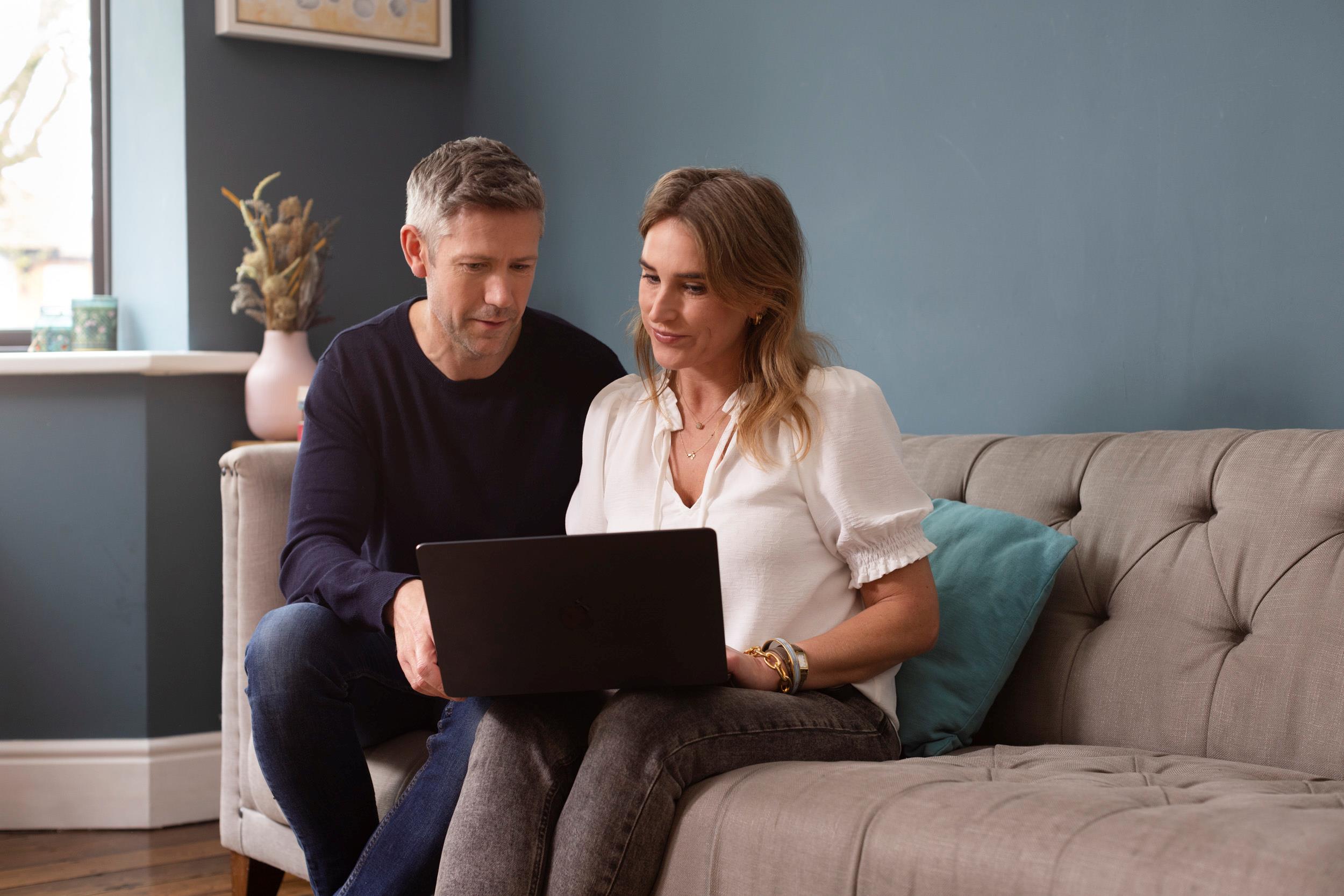 A couple sitting on a couch looking at a laptop