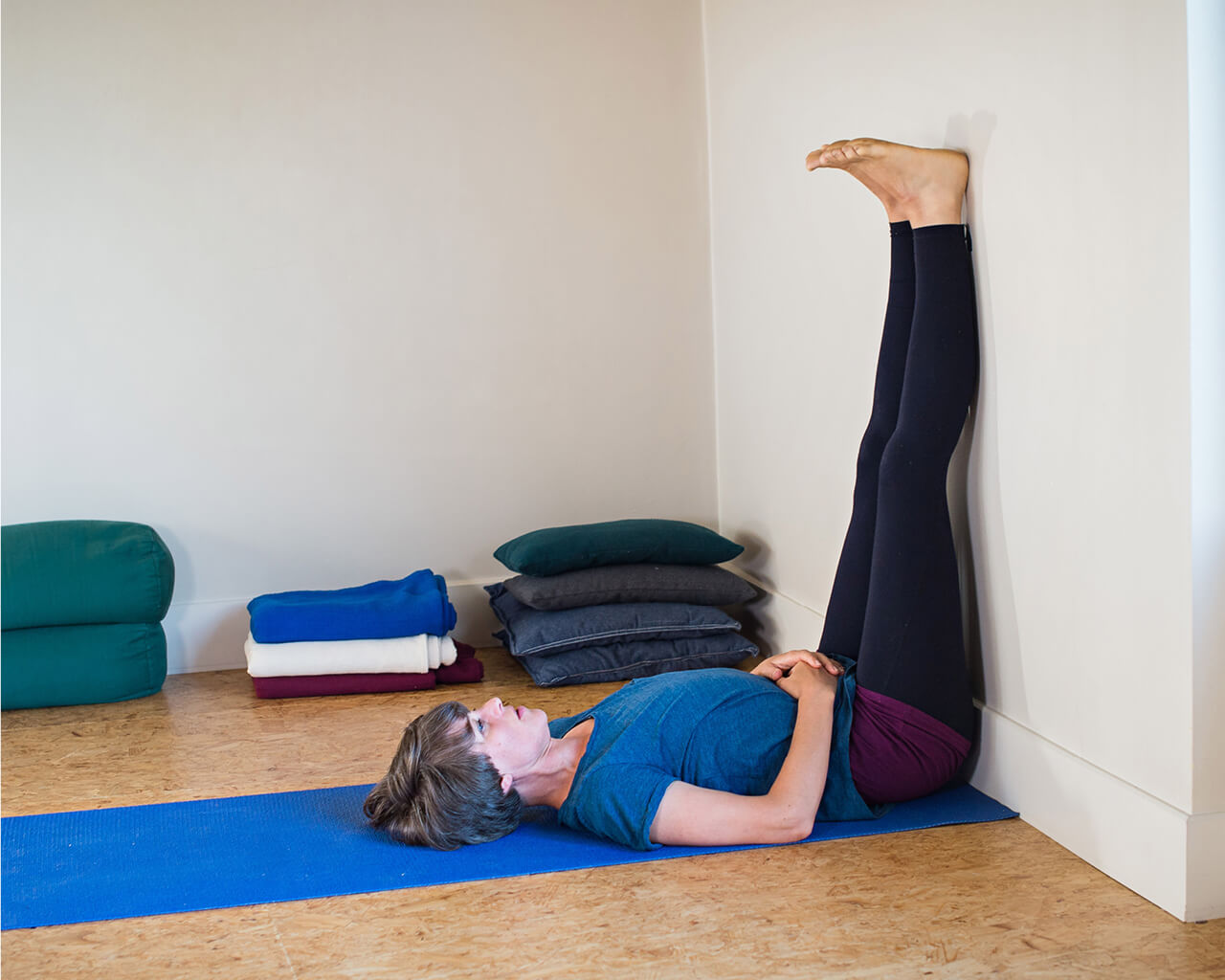 Jessica Hatchet lying on a yoga mat on the floor with her legs up against a wall