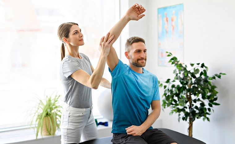 man during physiotherapy session sitting on a table and woman is raising his arm